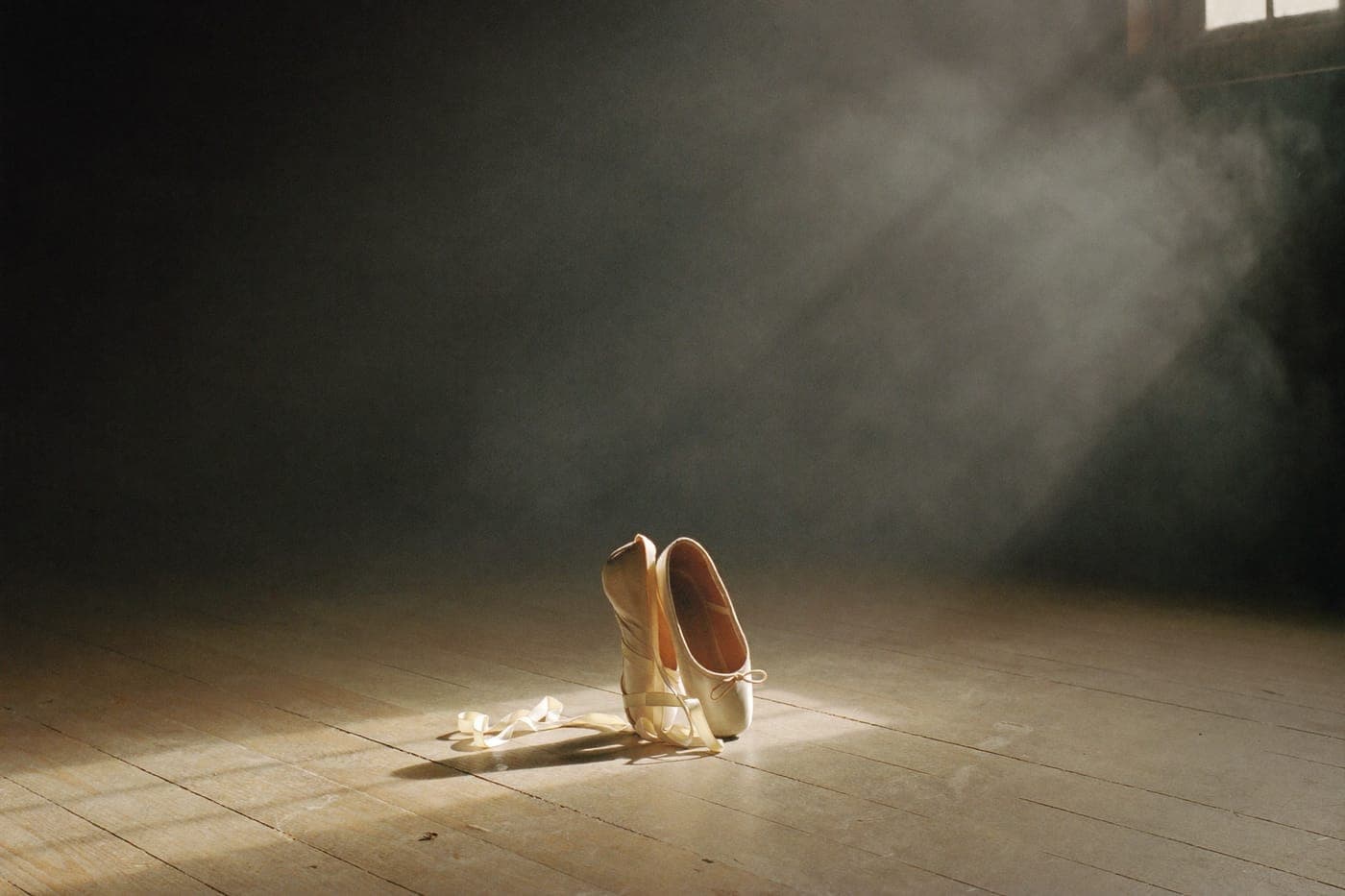 Worn ballet pointe shoes with ivory silk ribbons on an old theatre stage floor
