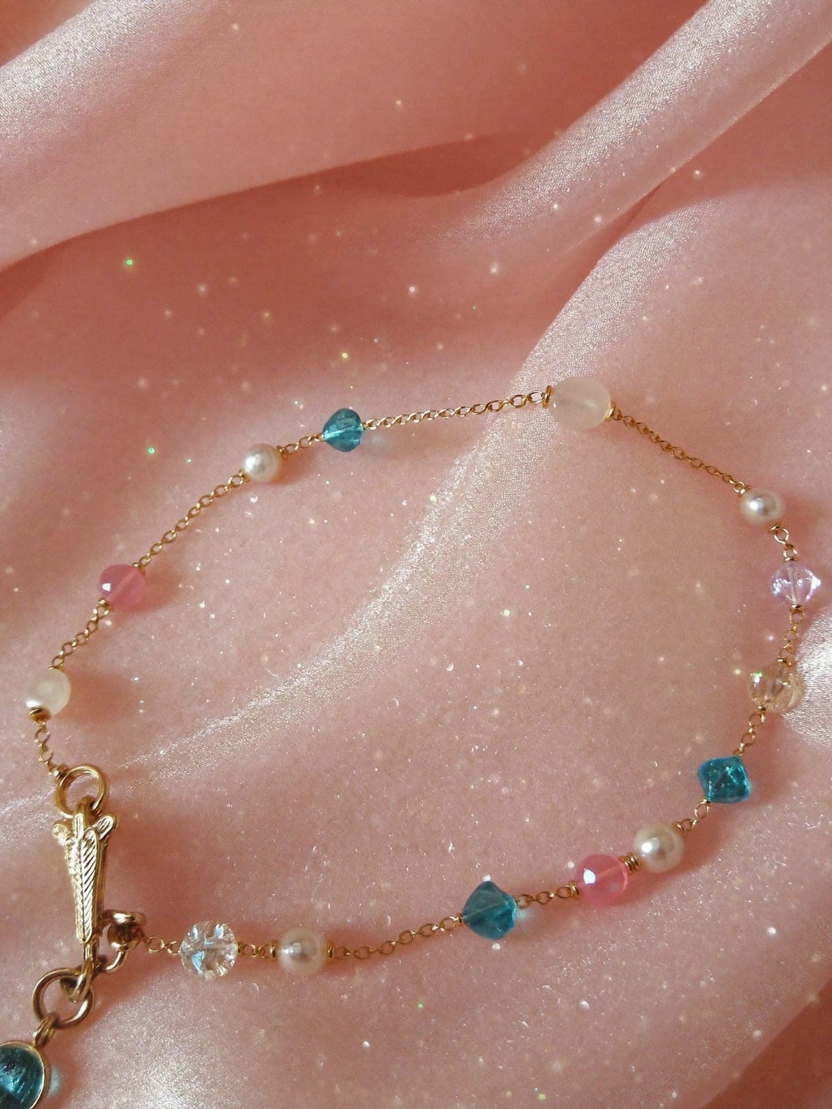 Delicate gold bracelet with moonstone and pearl beads on rain-wet slate by still water