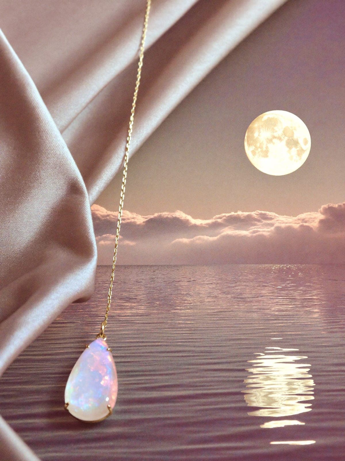 Teardrop moonstone pendant on a fine gold chain over wet dark stone by moonlit water